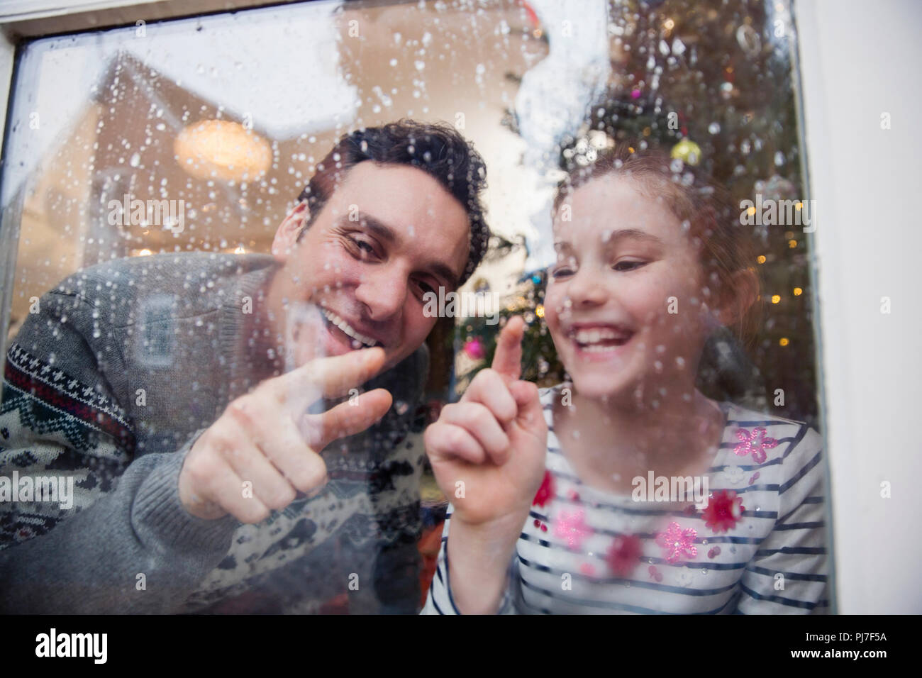 Father and daughter drawing in condensation on wet winter window Stock Photo