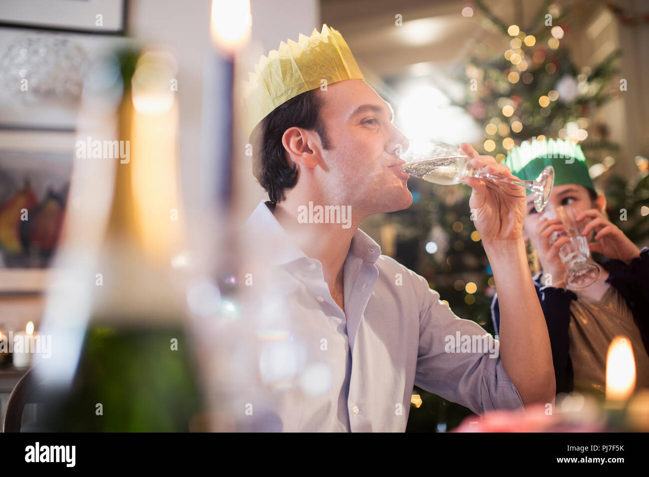 Daughter watching happy father in paper crown drinking champagne at Christmas dinner Stock Photo