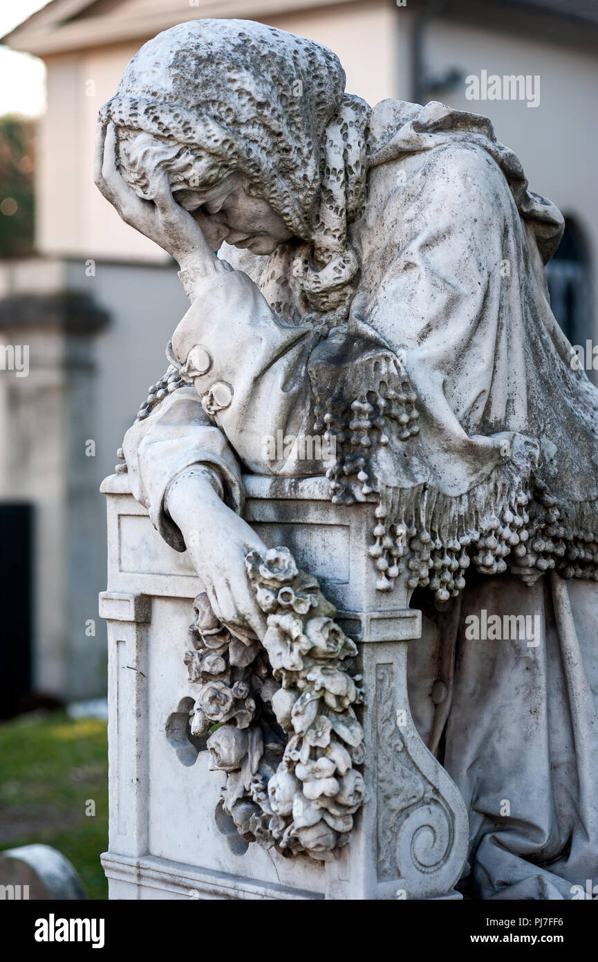 An old suffering woman statue cries on her knees onto the tombstone
