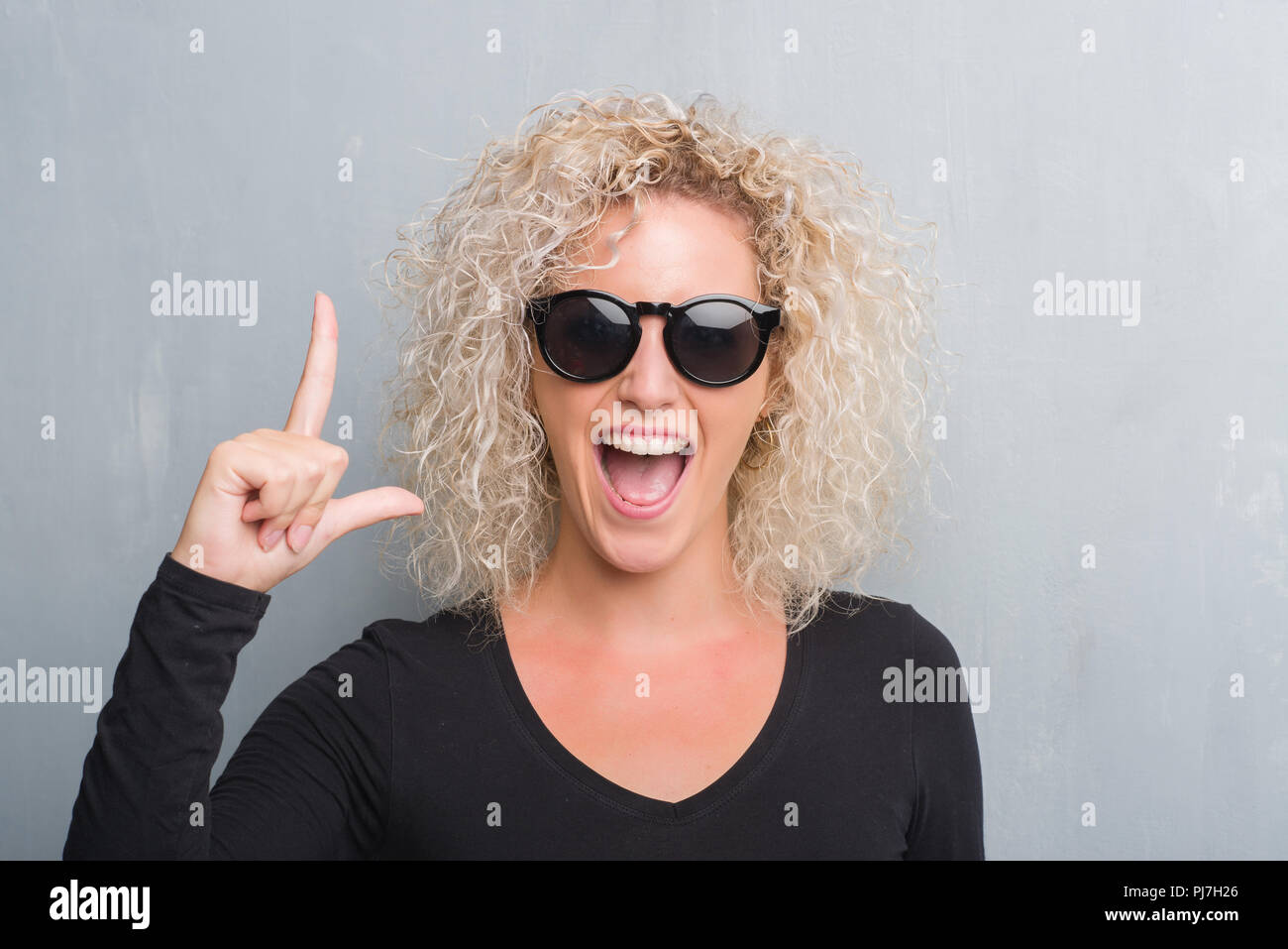 Young blonde woman with curly hair over grunge grey background pointing ...