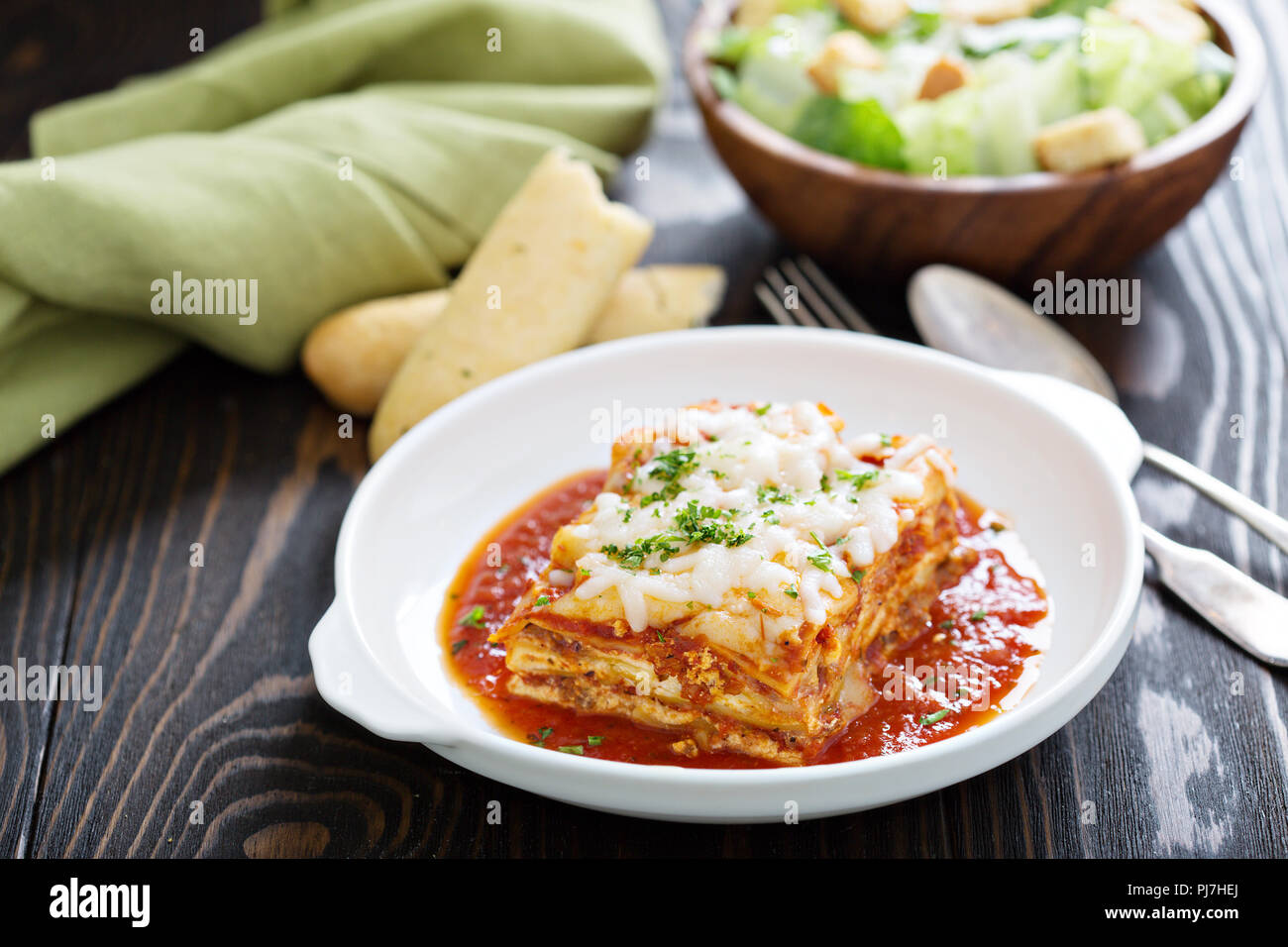 Traditional lasagna on white plate with caesar salad and breadsticks