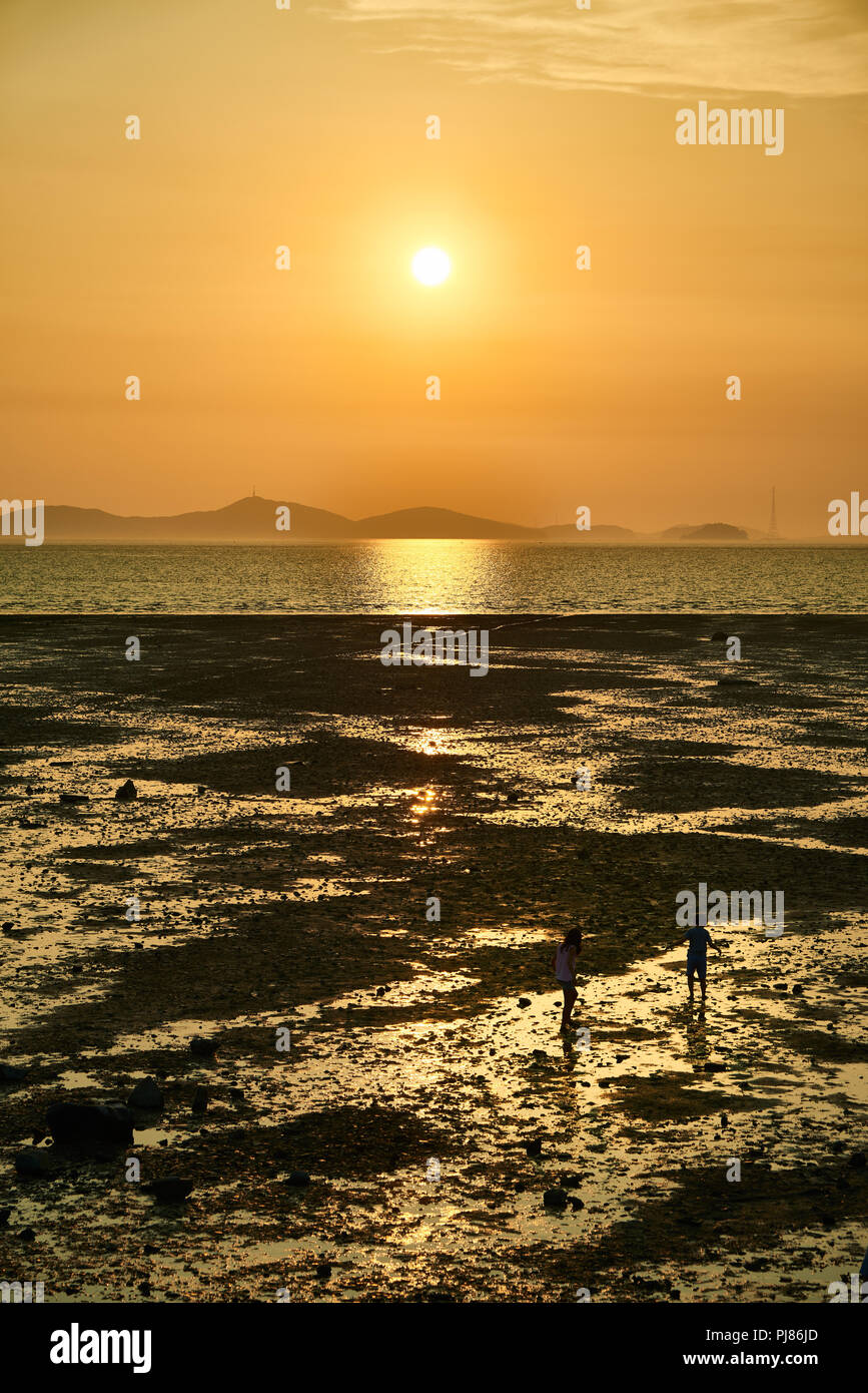 Ganghwa-gun, Korea - August 03, 2018: Sunset above horizon and children on mudflat in Janghwa-ri sunset viewing point. The place is famous for its stu Stock Photo