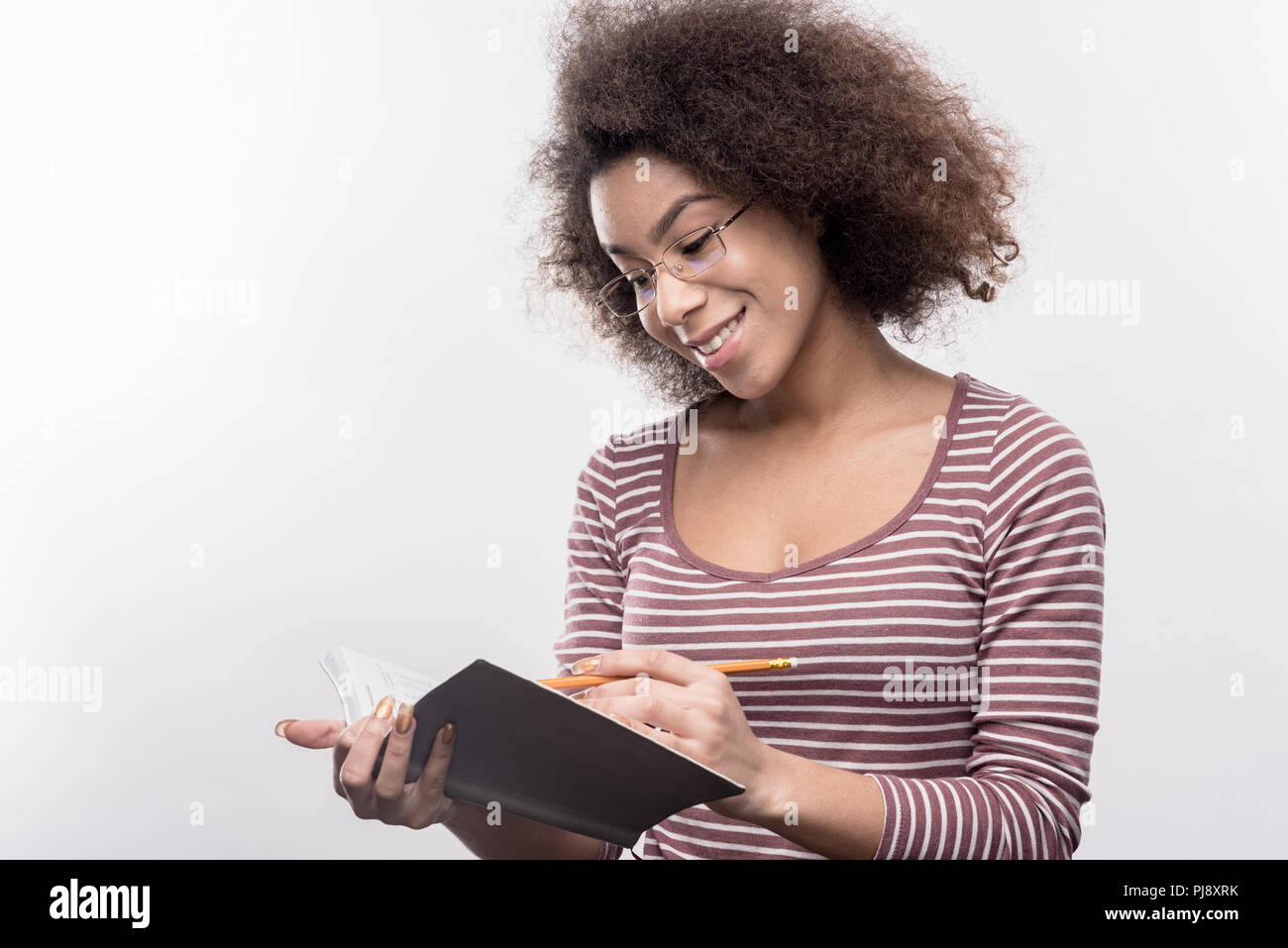 Clever dark-haired curly student doing her homework making some notes Stock Photo