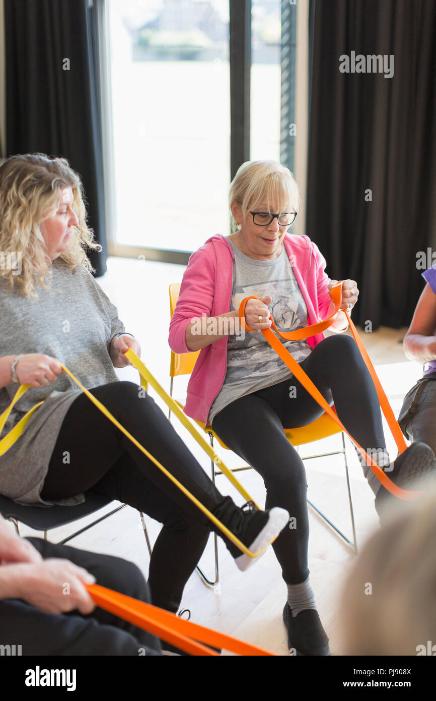 Active senior woman exercising, stretching leg with strap in exercise class Stock Photo