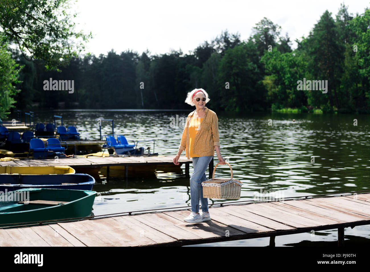 Elderly woman wearing glasses holding hamper for picnic in hand Stock