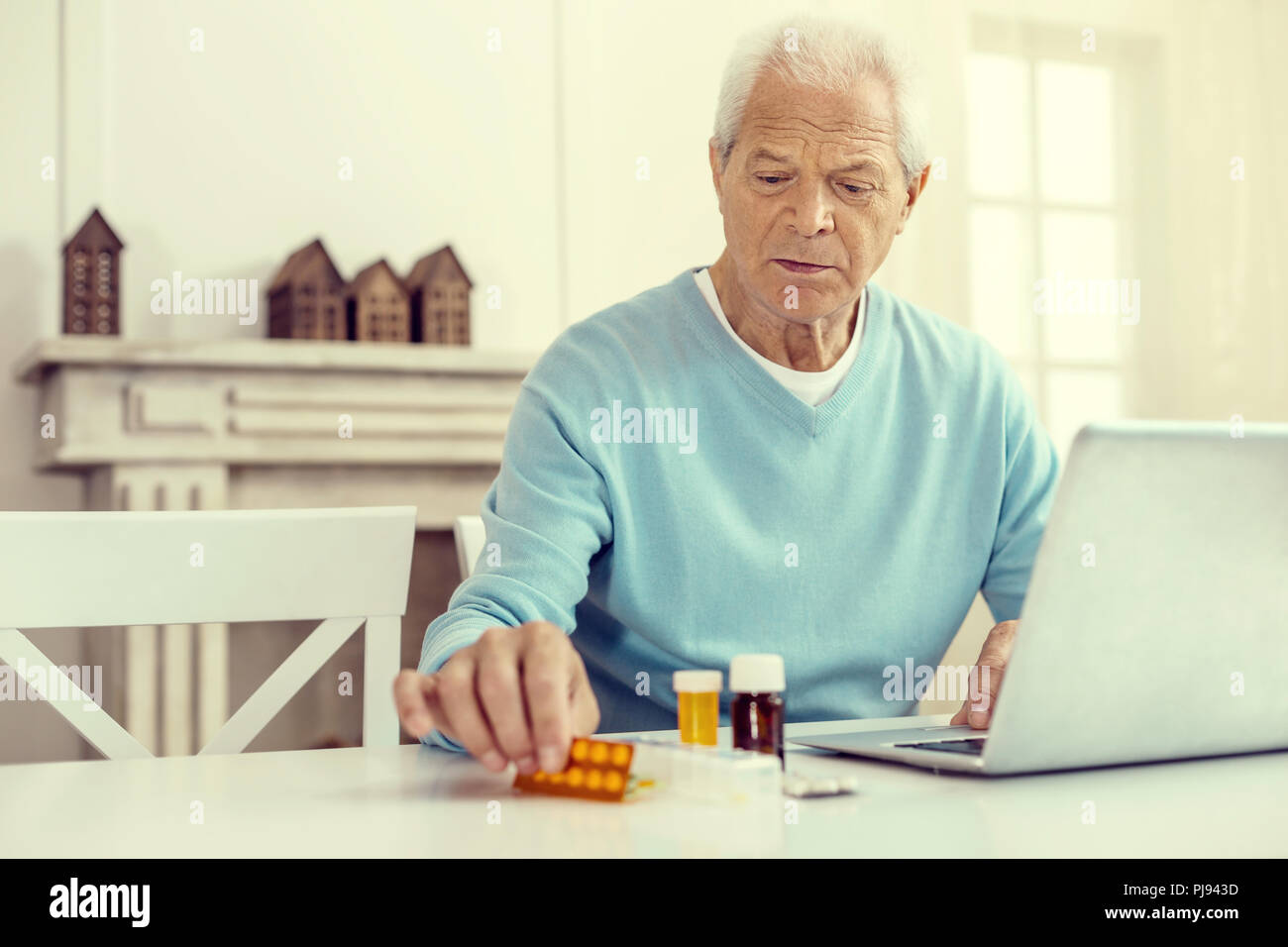 Upset retired man taking his pills while working on laptop Stock Photo