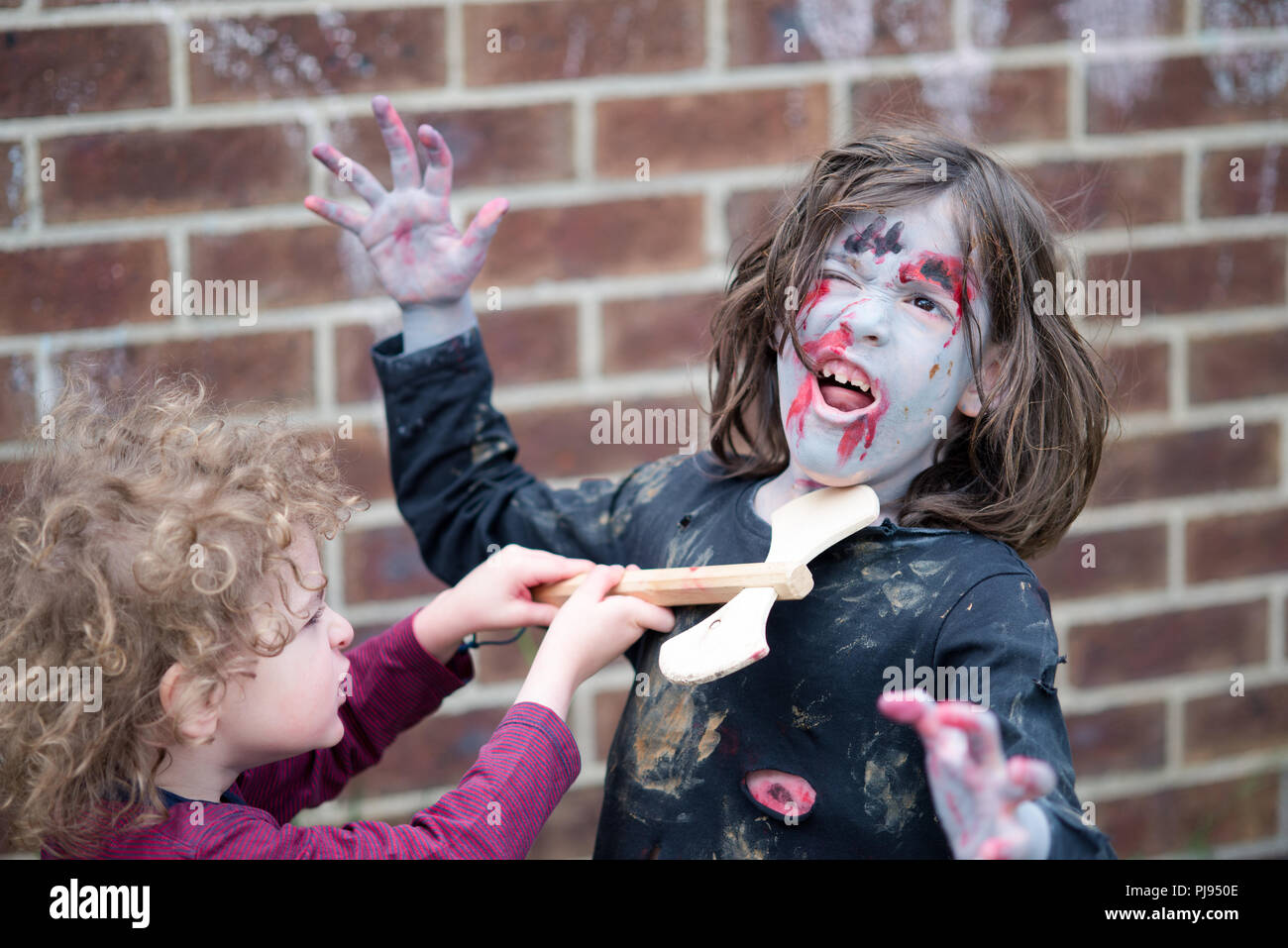 Boy with wooden axe attacks zombie girl for Halloween children zombie cosplay Stock Photo