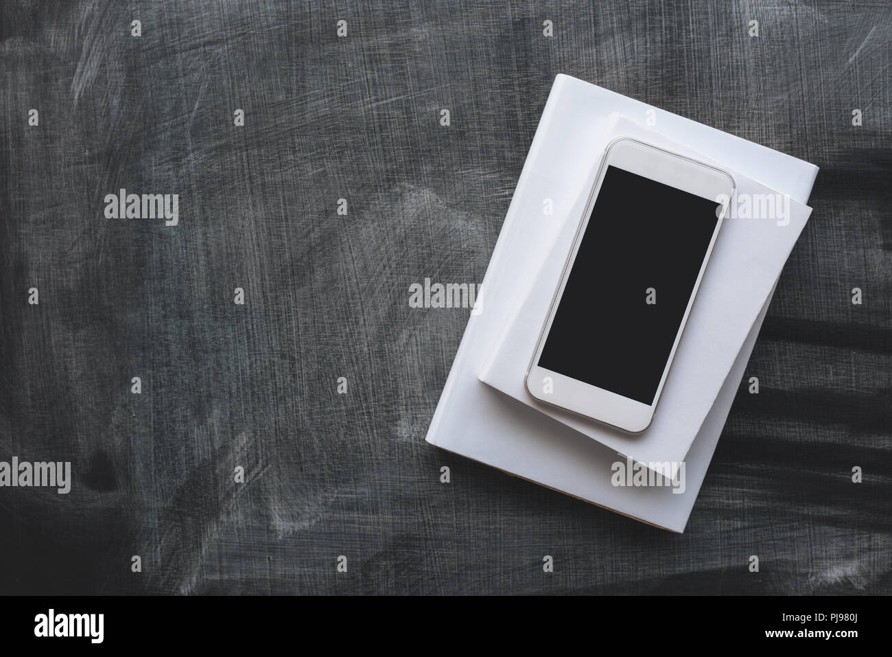 Smartphone with mock up screen on top of school books over blackboard Stock Photo