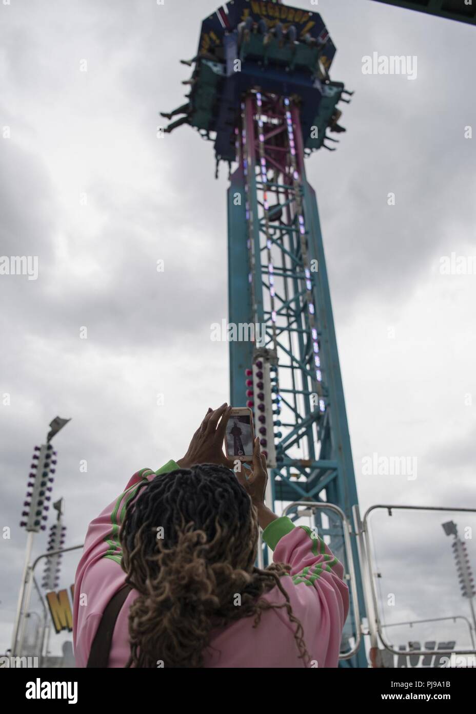 A spectator takes a picture of participants riding the “Mega Drop” during the 3rd annual Summer Fest hosted by the 673d Force Support Squadron at Joint Base Elmendorf-Richardson, Alaska, July 8, 2018. The event was open to anyone with base access and offered free activities such as carnival rides, a petting zoo, face painting, a bungee trampoline, and carnival games. Stock Photo