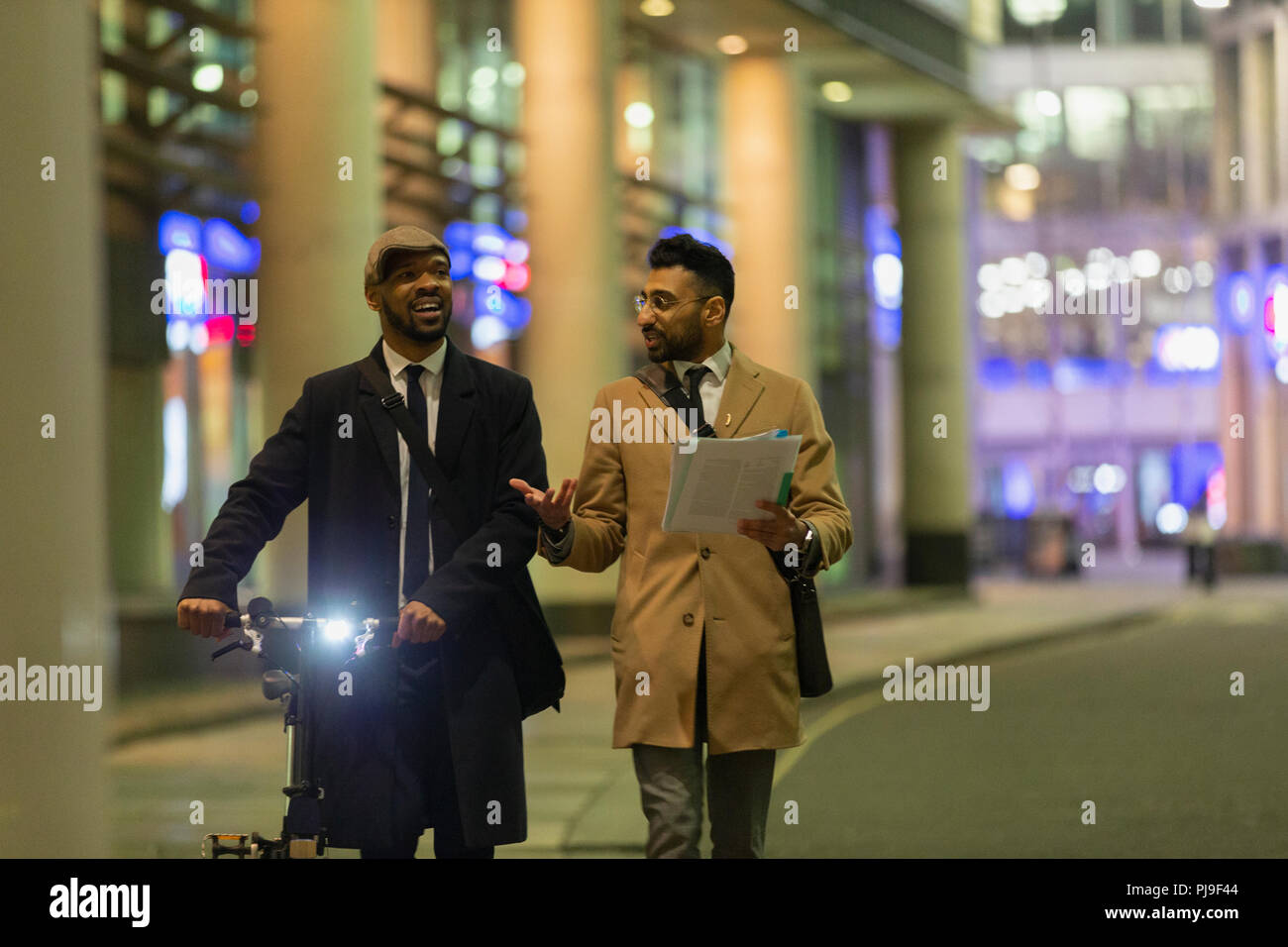 Businessmen talking, discussing paperwork on urban sidewalk at night Stock Photo