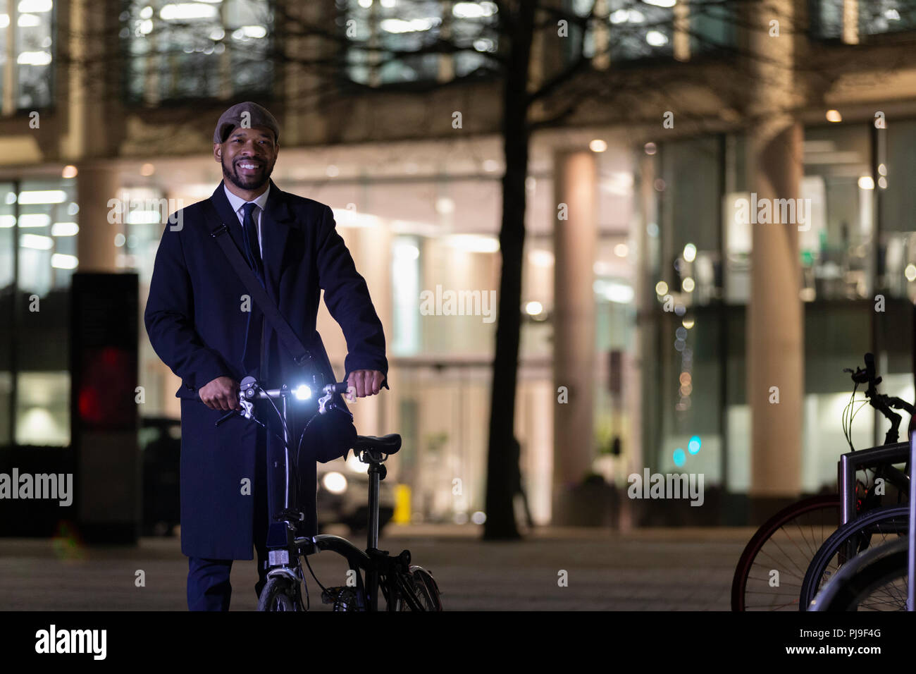 Portrait confident businessman with bicycle on urban street at night Stock Photo