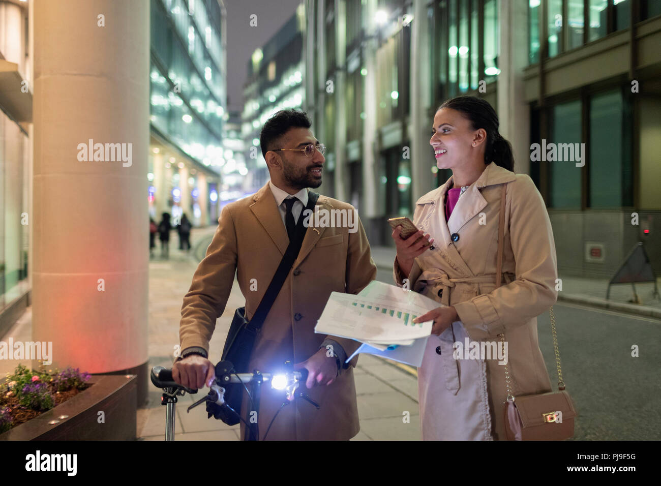 Business people discussing paperwork on urban sidewalk at night Stock Photo