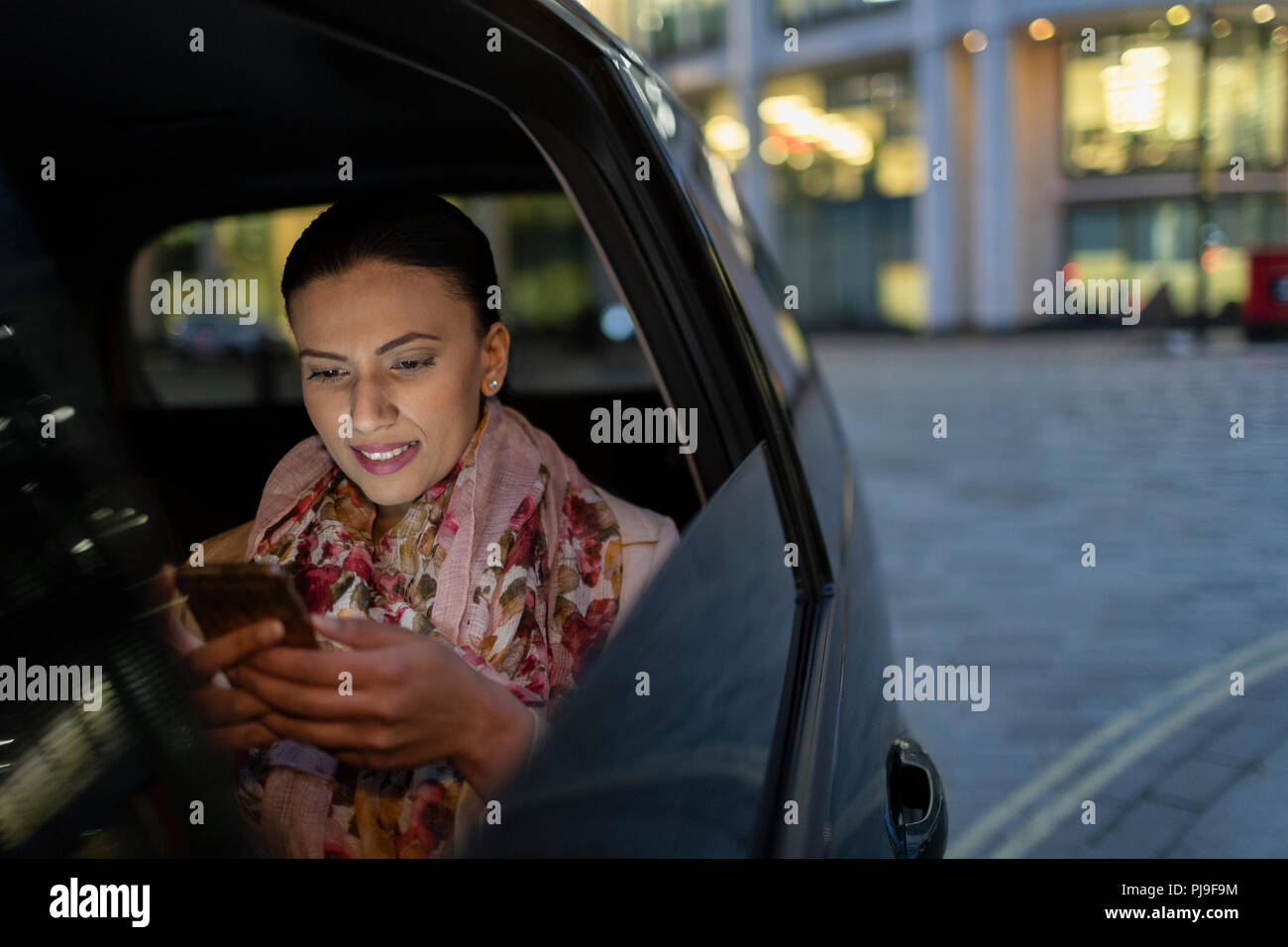 Businesswoman using smart phone in crowdsourced taxi at night Stock Photo