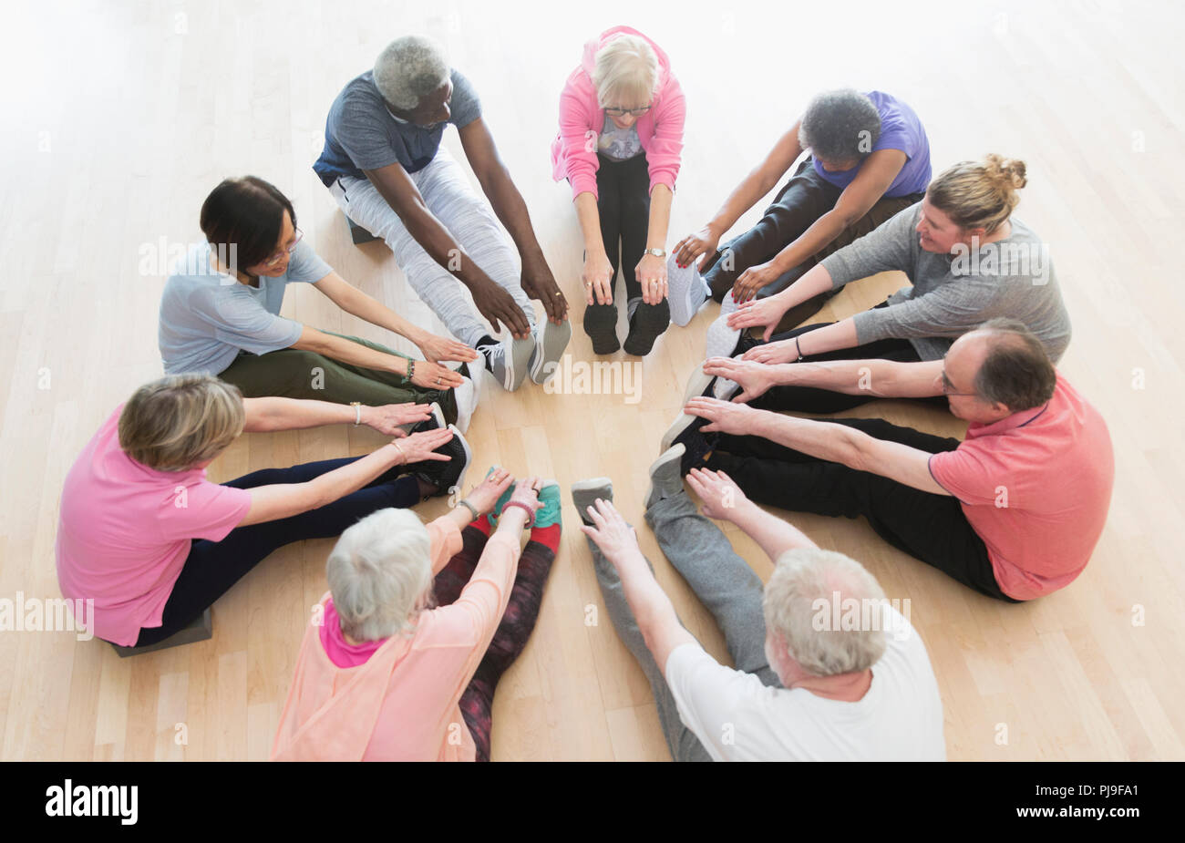 Active seniors stretching legs in circle in exercise class Stock Photo
