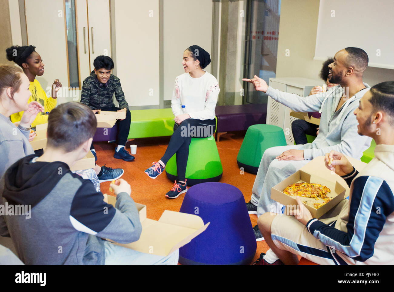 Teenagers and mentor talking and eating pizza in community center Stock Photo