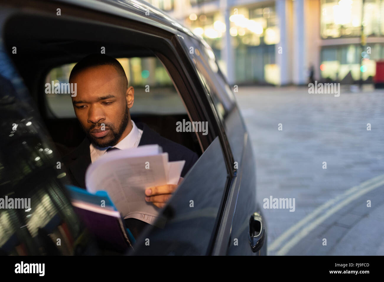 Businessman reading paperwork in crowdsourced taxi at night Stock Photo