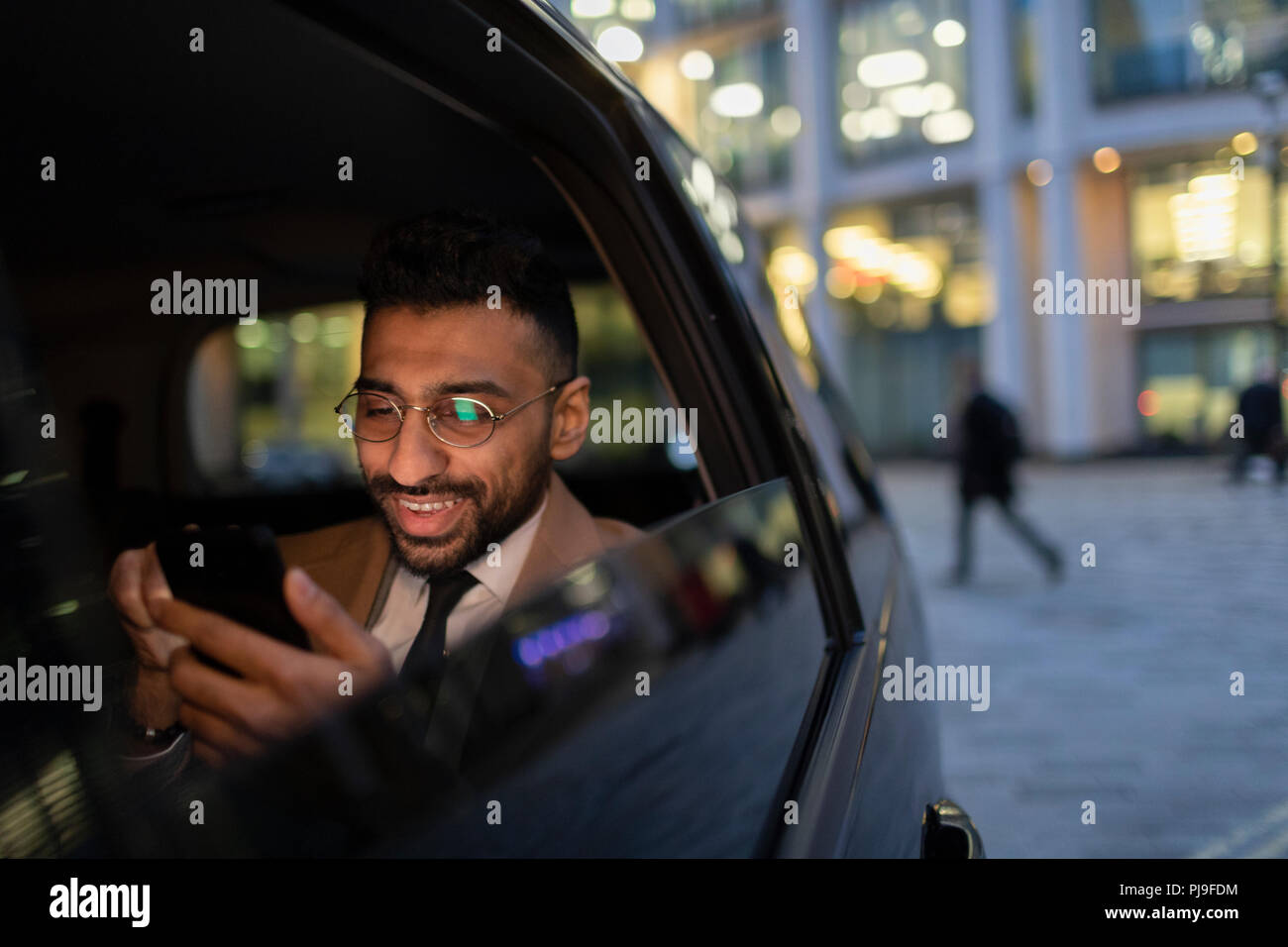 Businessman using smart phone in crowdsourced taxi at night Stock Photo