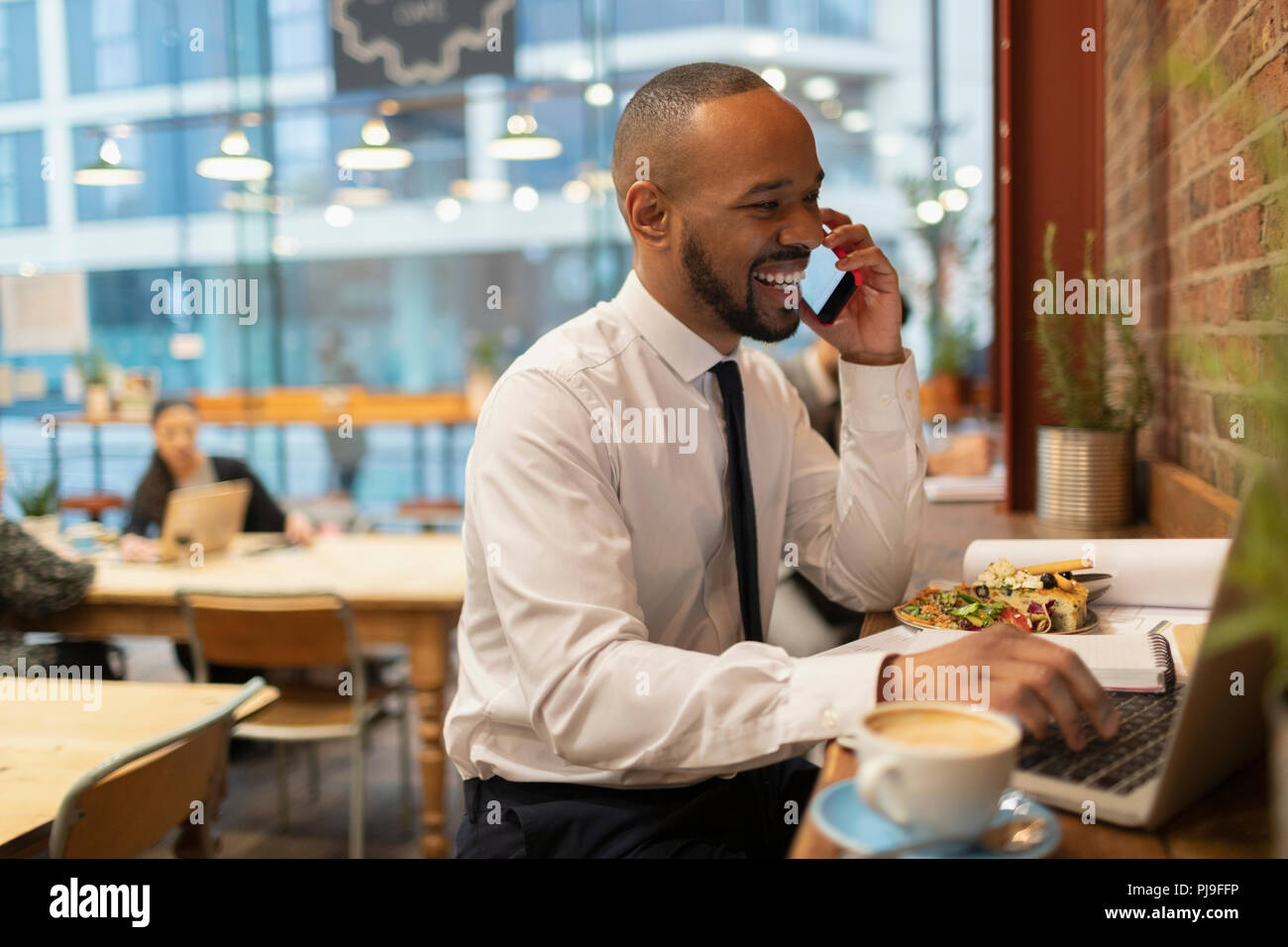 Smiling businessman talking on smart phone, working in cafe Stock Photo