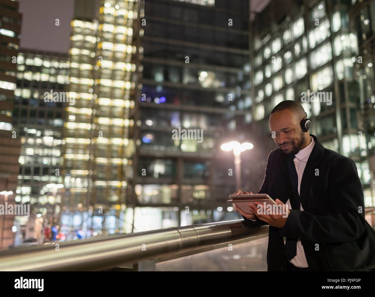 Businessman with headphones using digital tablet on urban pedestrian bridge at night Stock Photo