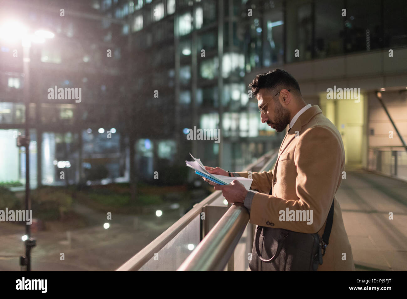 Businessman reviewing paperwork on urban pedestrian bridge at night Stock Photo