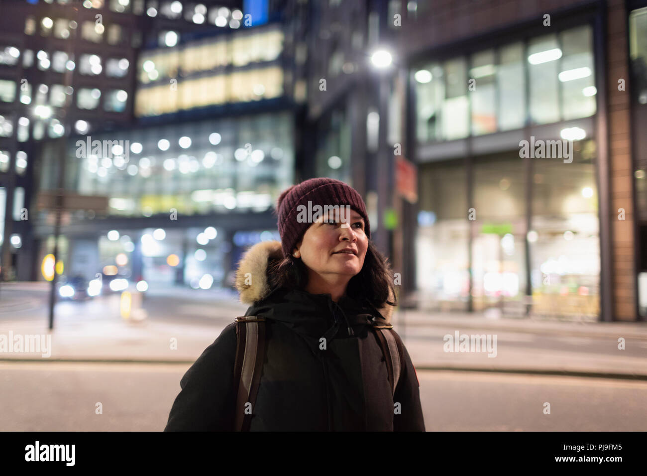 Woman in warm clothing walking on urban street at night Stock Photo