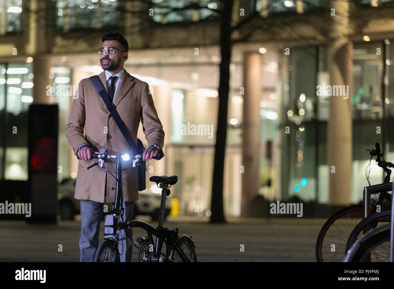 Businessman with bicycle on urban street at night Stock Photo