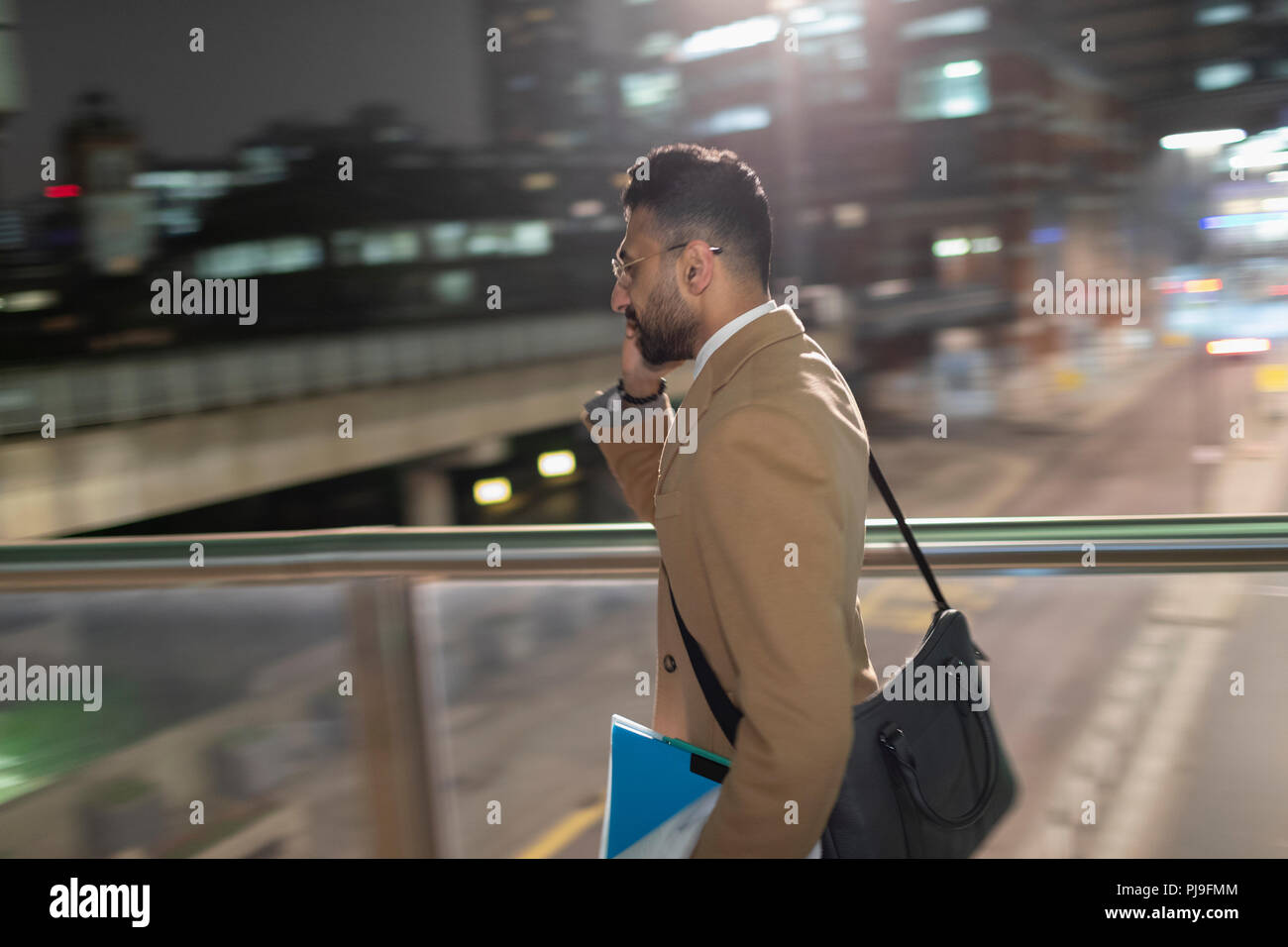 Businessman talking on smart phone, walking on urban pedestrian bridge at night Stock Photo