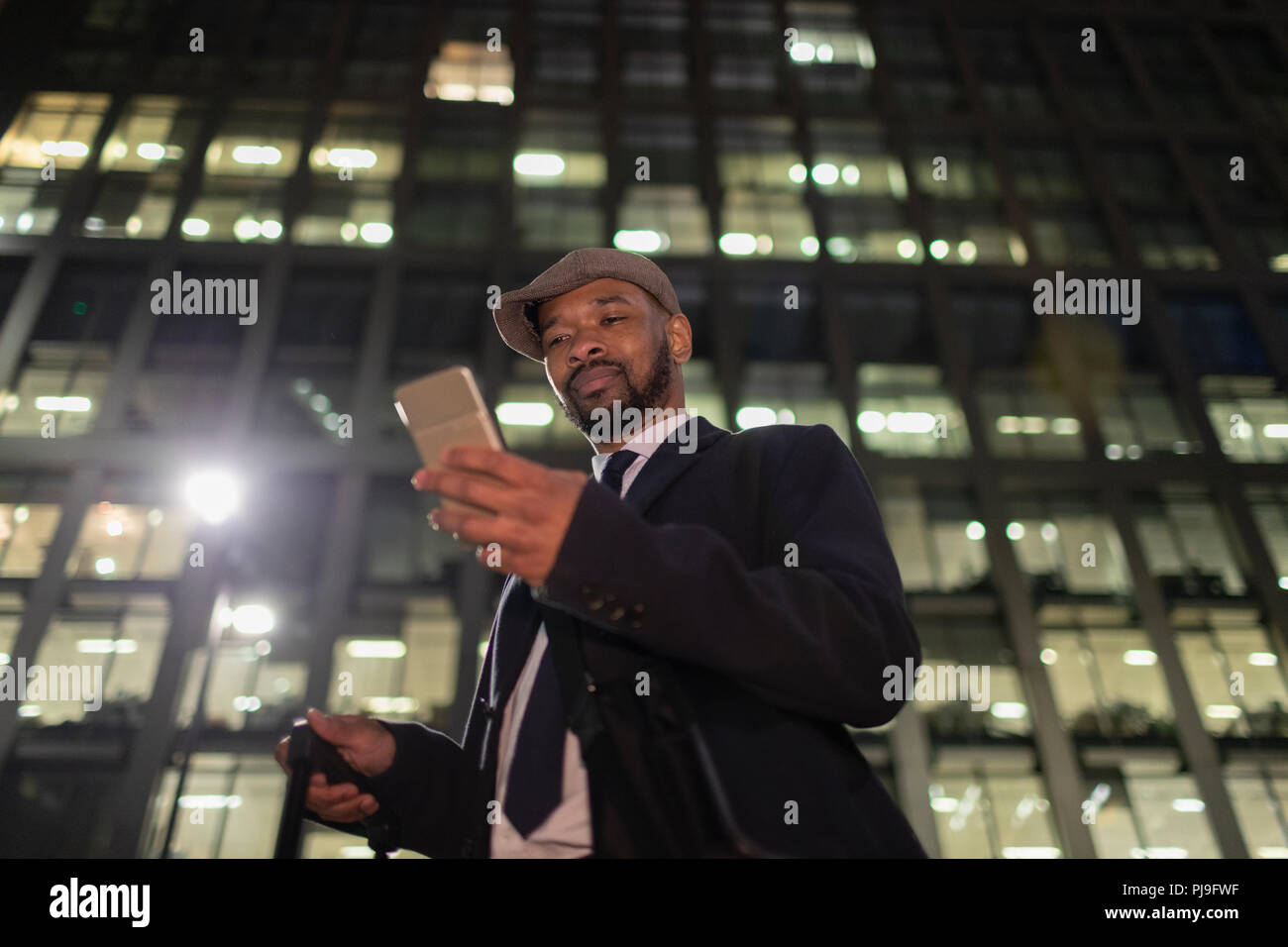 Businessman with smart phone standing below urban highrise at night Stock Photo