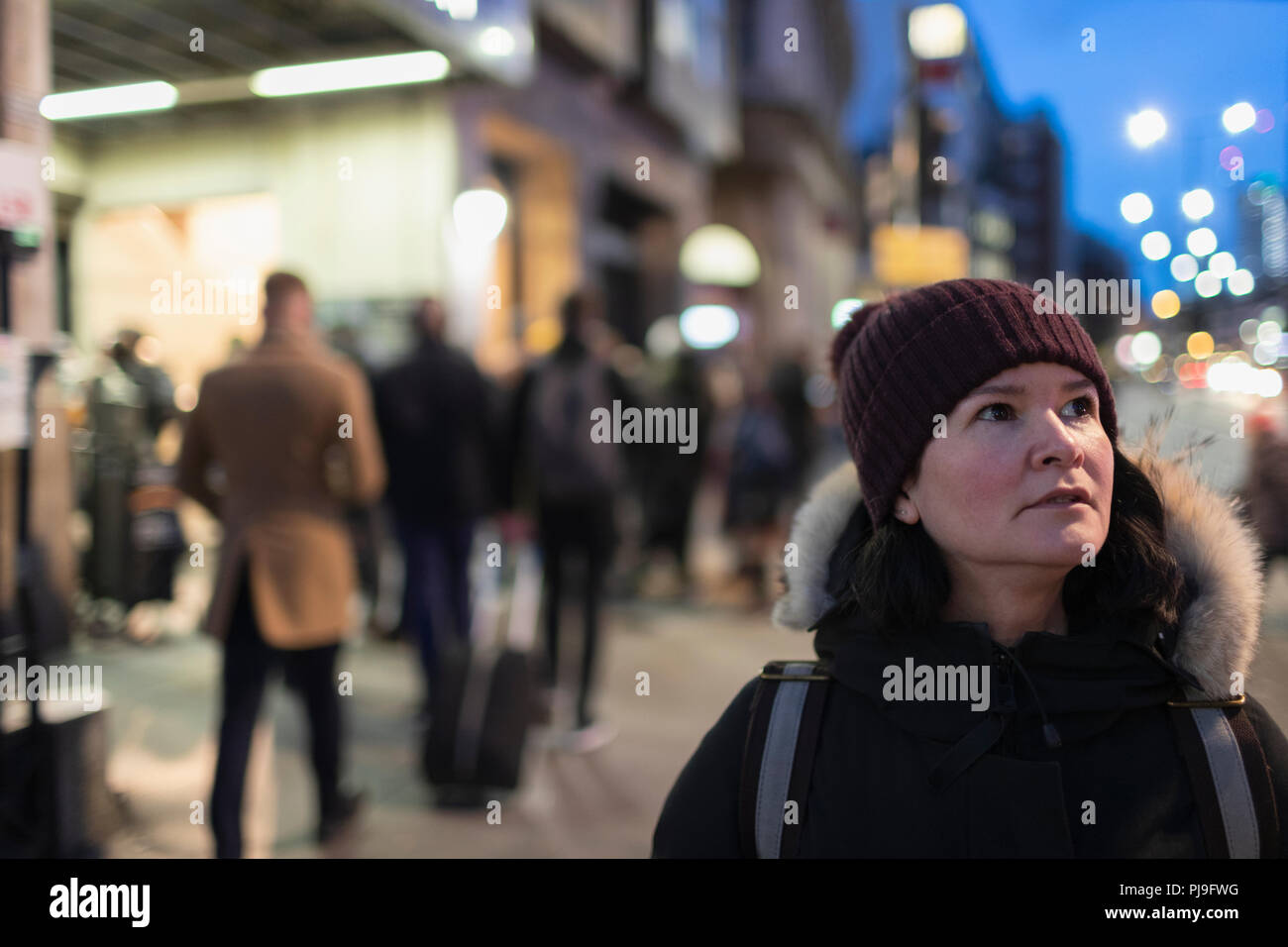 Woman in warm clothing standing on urban sidewalk at night Stock Photo