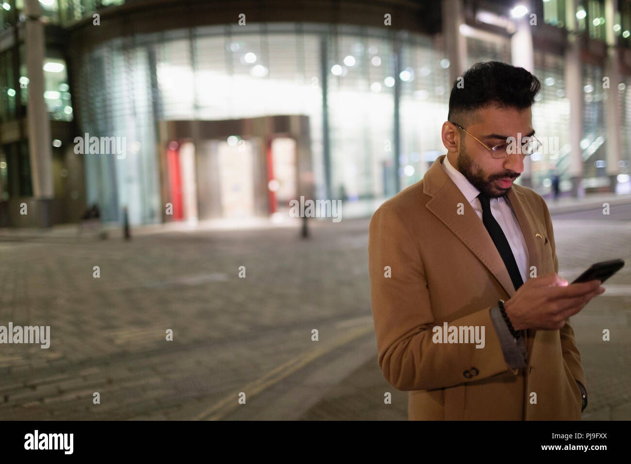 Businessman texting with smart phone on urban street corner at night Stock Photo