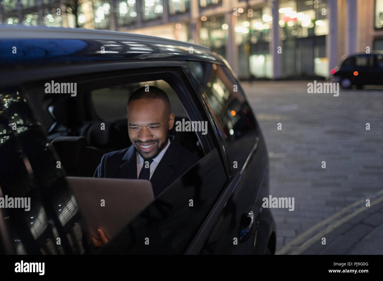 Smiling businessman using laptop in crowdsourced taxi at night Stock Photo