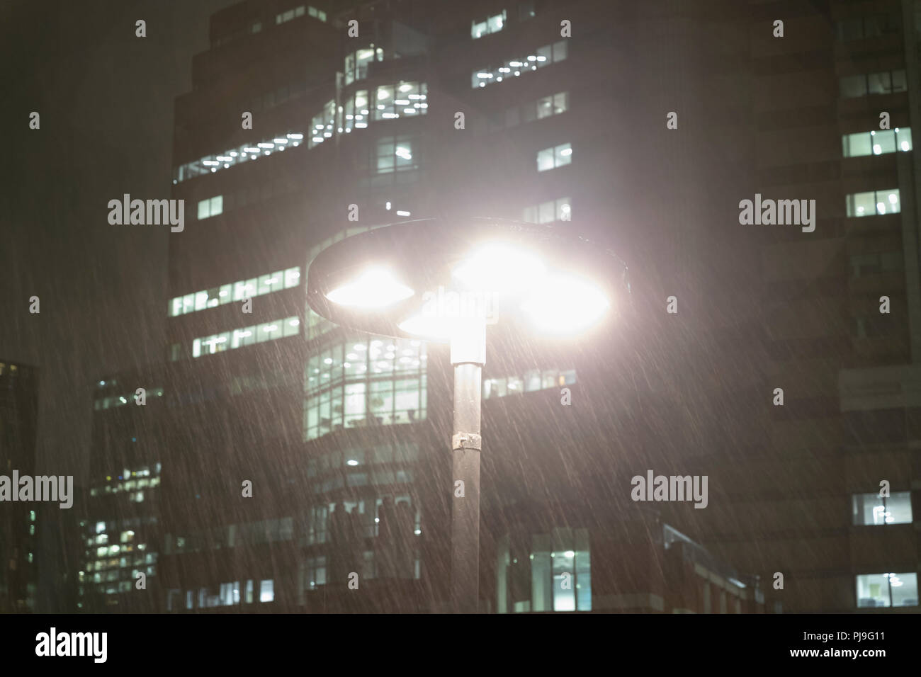 Rain falling around streetlamp below urban highrise buildings at night Stock Photo