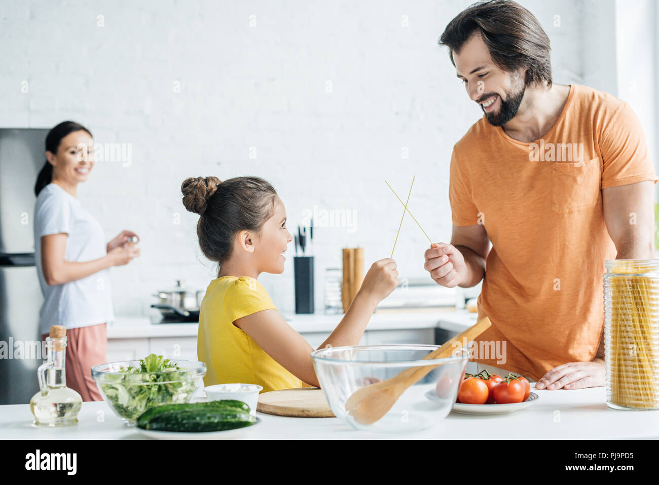 father and daughter playing with chopsticks while mother standing blurred on background at kitchen Stock Photo