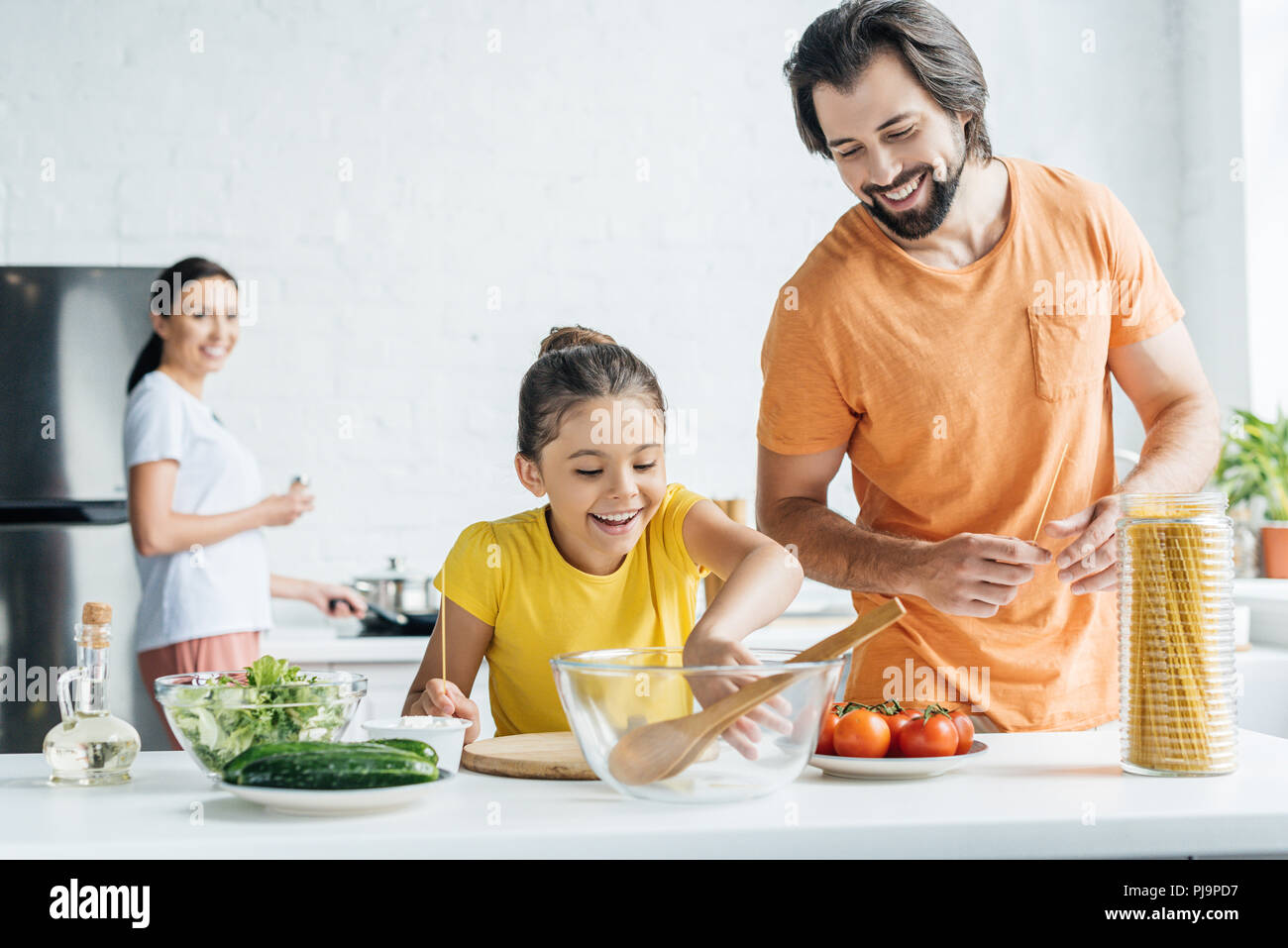 father and daughter cooking while mother standing blurred on background at kitchen Stock Photo