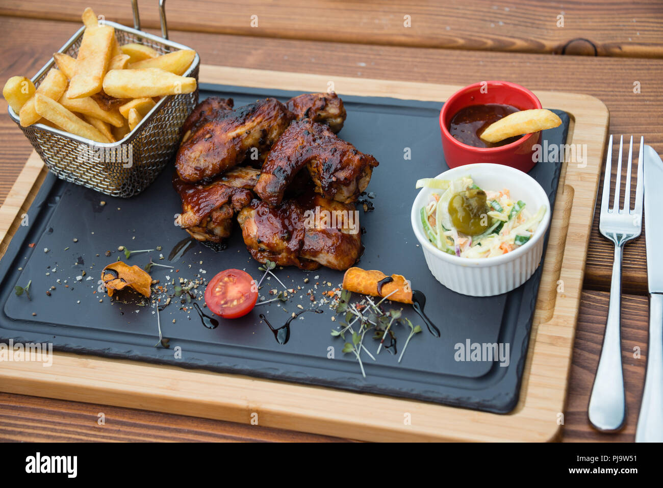 Delicious BBQ chicken wings served with Coleslaw salad and french fries on cutting board Stock Photo