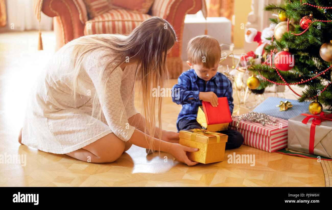 Cute 3 years old boy sitting under Christmas tree and looking inside