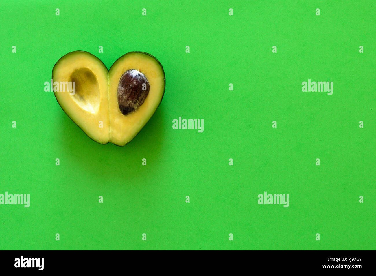 Heart-shaped slices of avocado on green background Stock Photo