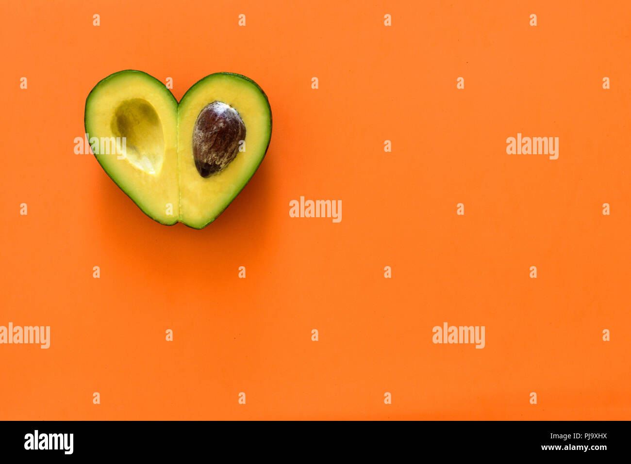 Heart-shaped slices of avocado on orange background Stock Photo