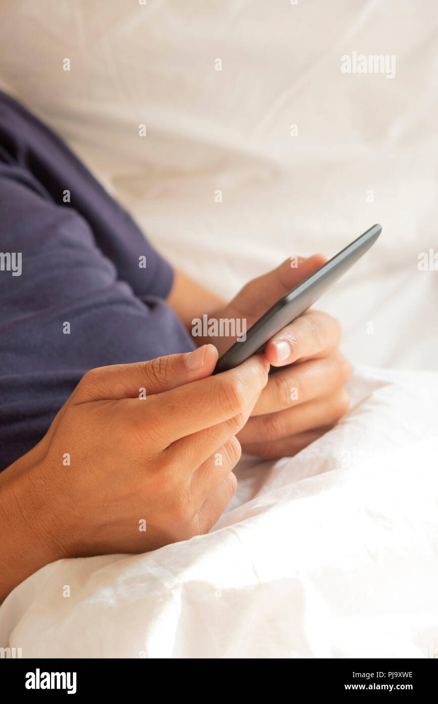 closeup of a young caucasian man in pajamas using a digital tablet or an e-reader in bed Stock Photo