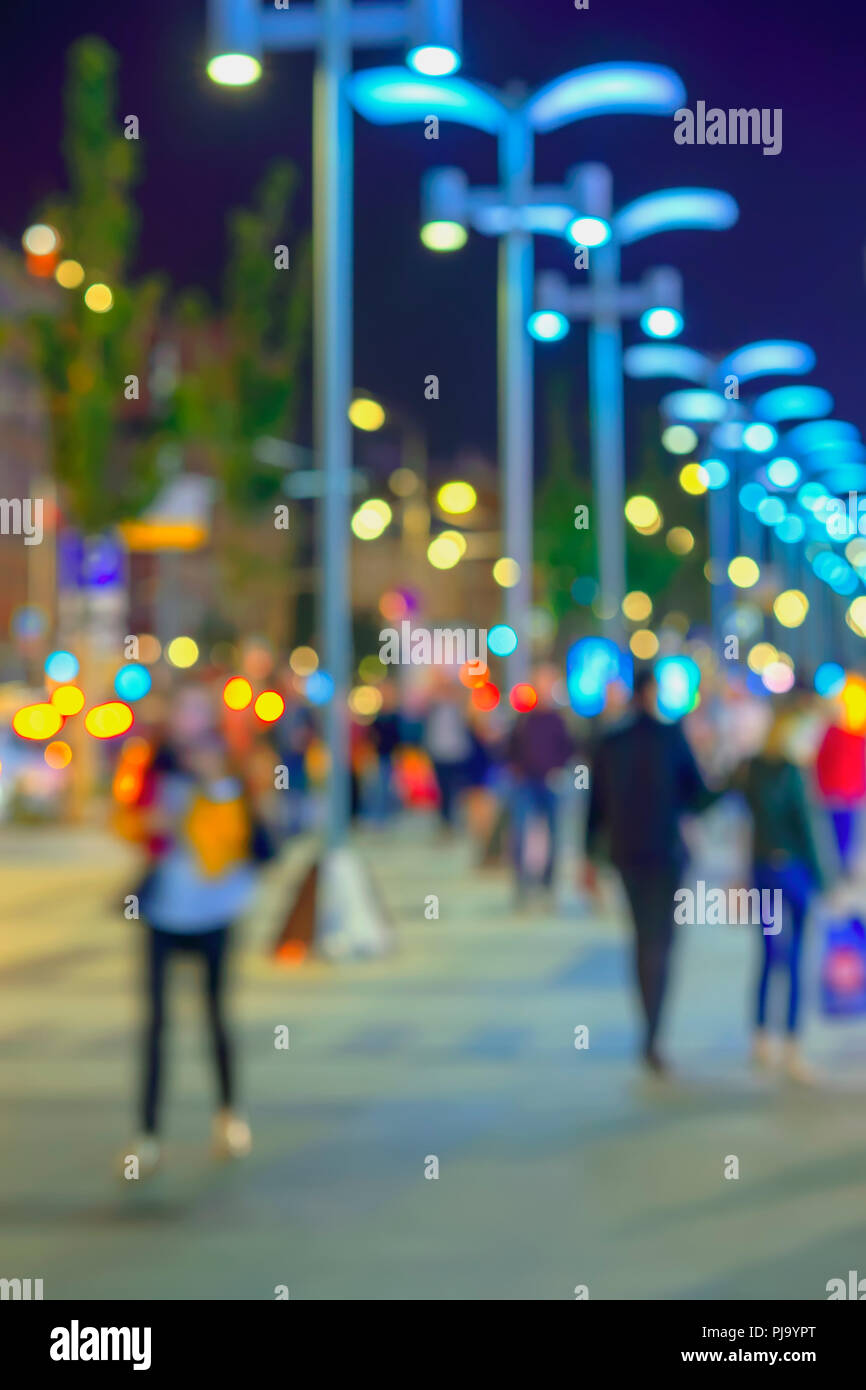 Abstract bright blurred background with bright bokeh, city street in  evening, unidentified people, defocused motion. Vivid illumination, shop  windows and street lamps. Concept of seasons, modern city, urban lifestyle,  leisure Stock Photo -