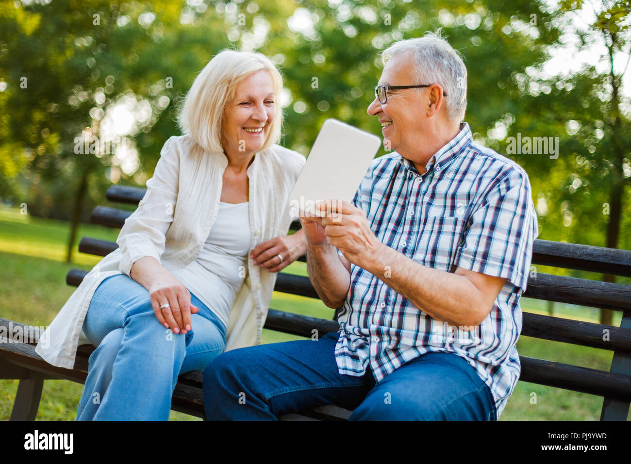 Happy senior couple is using digital tablet in park. Stock Photo