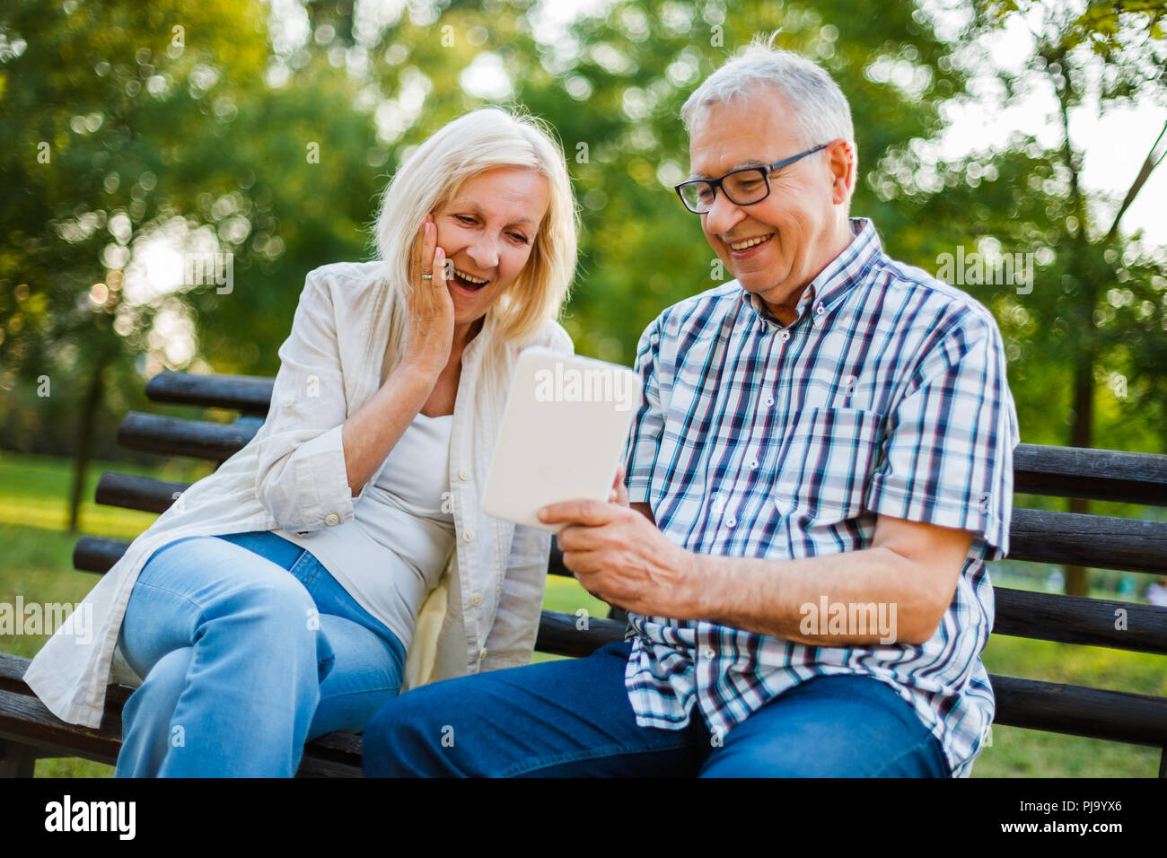 Happy senior couple is using digital tablet in park. Stock Photo