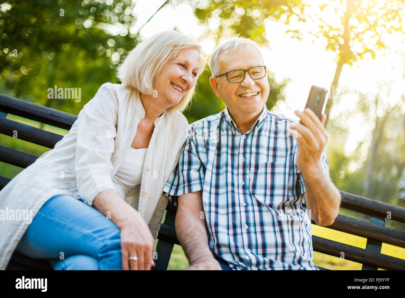 Happy senior couple is using smartphone in park. Stock Photo