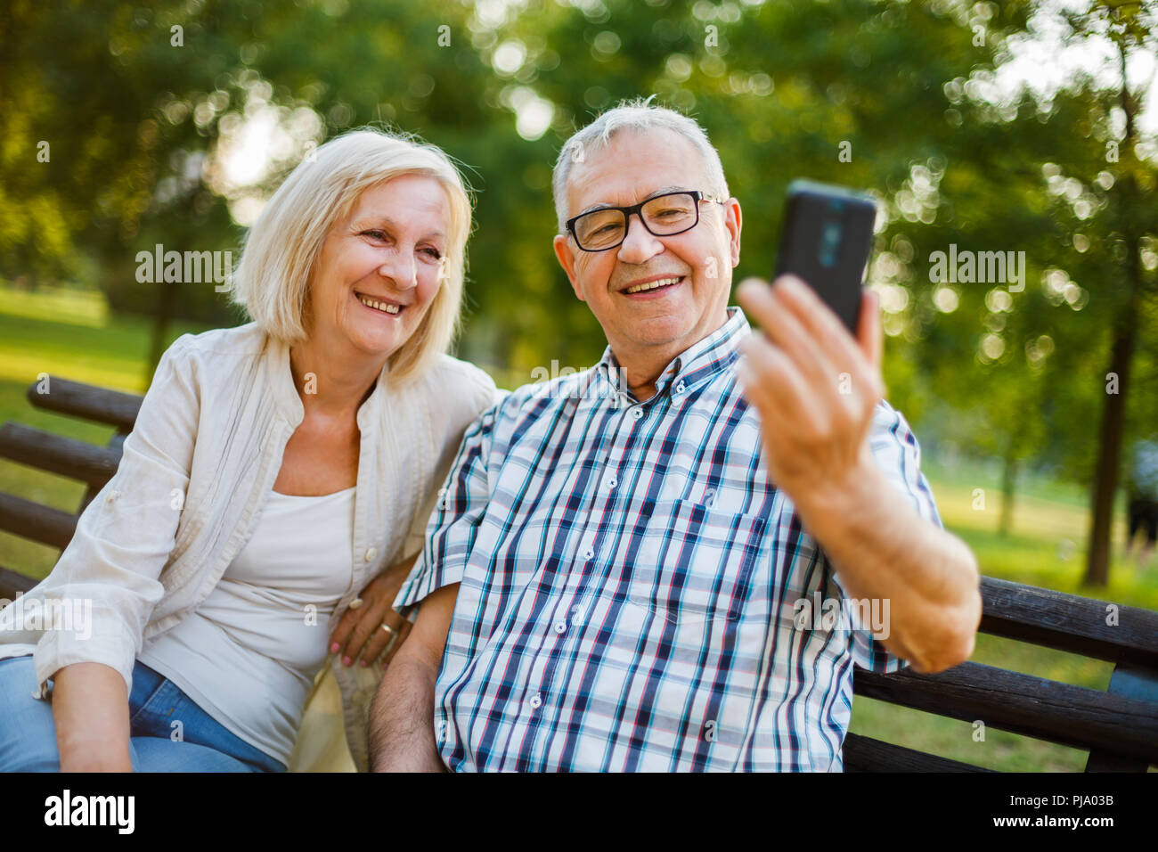 Happy senior couple is using smartphone in park. Stock Photo