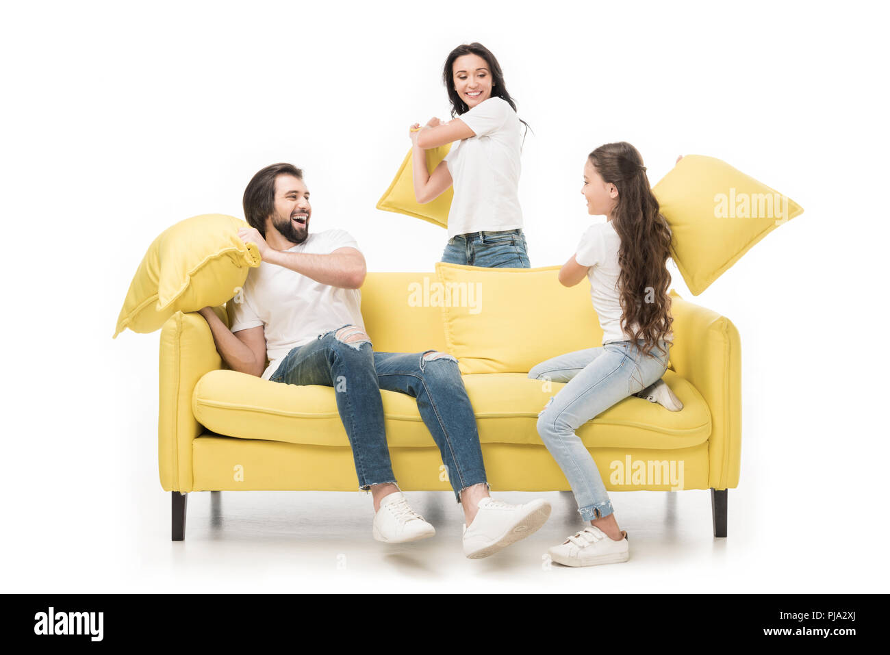 happy family in white shirts on yellow sofa having pillow fight isolated on white Stock Photo