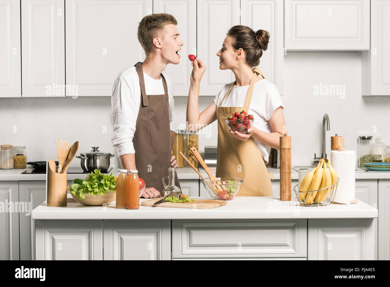 girlfriend feeding boyfriend with strawberry in kitchen Stock Photo - Alamy