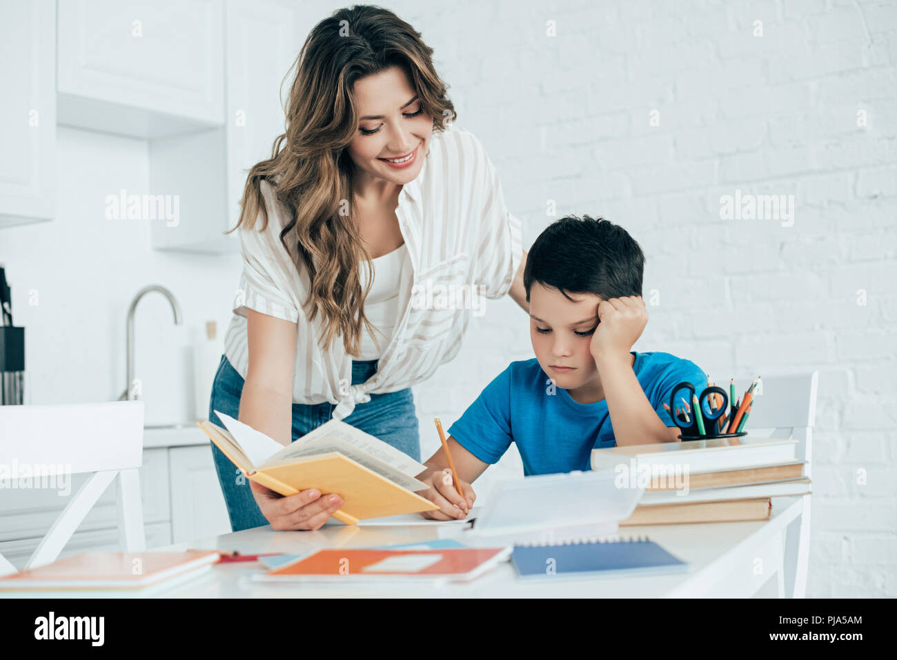 portrait of mother helping bored son with homework in kitchen at home ...