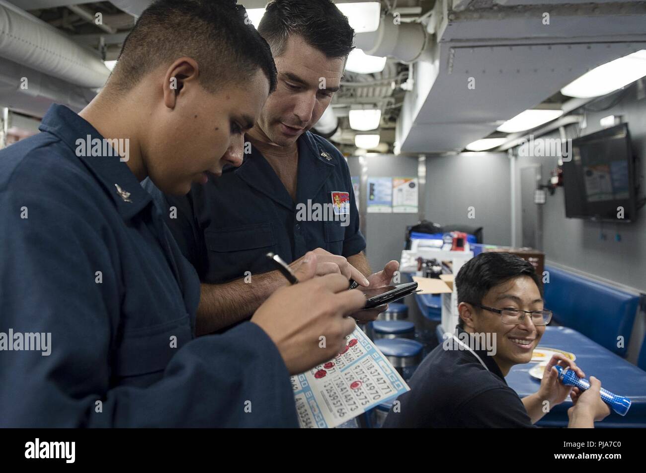 PHILIPPINE SEA (July 4, 2018) Fire Controlman (Aegis) 2nd Class Ismael Rodriguez, left, and Sonar Technican (Surface) 1st Class Timothy Baker check a bingo board during a Morale, Welfare and Recreation (MWR) event on the mess decks of the Arleigh Burke-class guided-missile destroyer USS Benfold (DDG 65). Benfold is forward-deployed to the U.S. 7th Fleet area of operations in support of security and stability in the Indo-Pacific region. Stock Photo