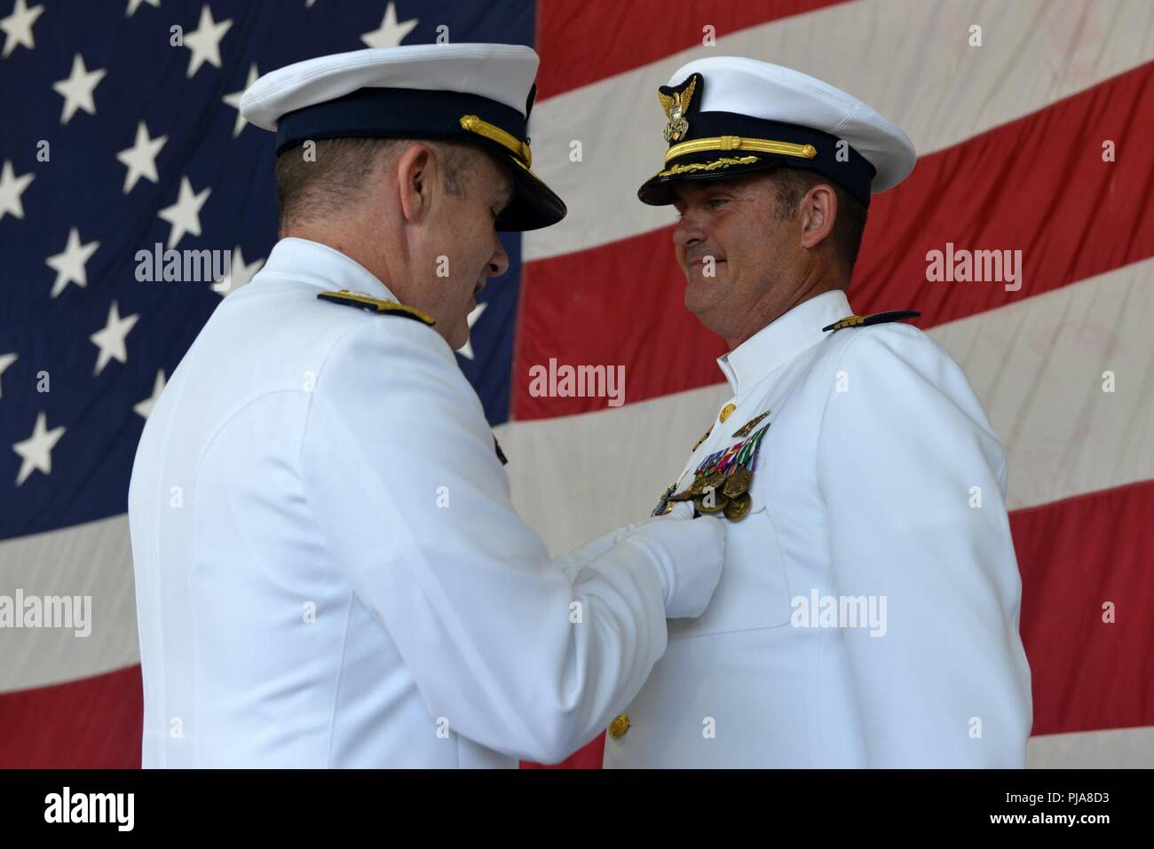 U.S. Coast Guard Capt. Frederick C. Riedlin is presented with a Meritorious Service Medal by Rear Adm. Brian Penoyer at Coast Guard Air Station Barbers Point, July 6, 2018. Riedlin received the medal at a change of command ceremony after which he is transferring to become the Coast Guard Chief of the Office of Aviation Forces (CG-711). Stock Photo