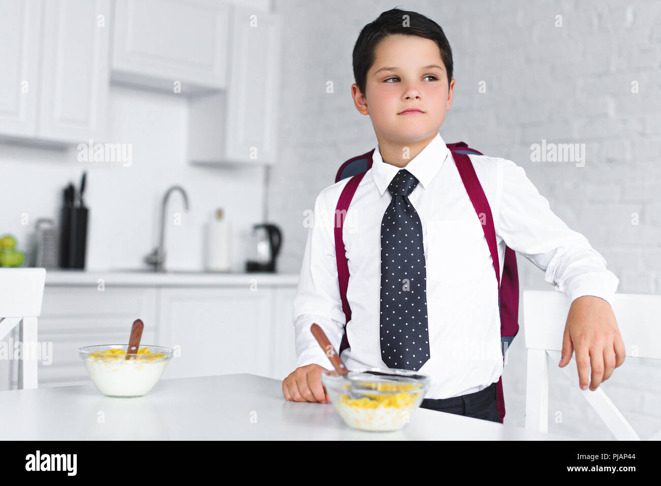portrait of pensive boy in school uniform with backpack standing at